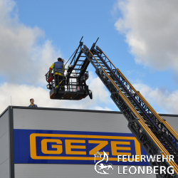 Am Samstagnachmittag veranstaltete die Freiwillige Feuerwehr Leonberg eine Gro&szlig;&uuml;bung bei der Firma GEZE, zu der auch die Bev&ouml;lkerung eingeladen war. Circa 350 Besucher beobachteten vom Betriebsparkplatz aus das interessante Geschehen, welches sich aus folgendem &Uuml;bungsszenario entwickelte:

Beim Be- und Entladen eines Lastwagens kommt es zu einem Unfall, in dessen Folge der LKW in Brand ger&auml;t. Das Feuer breitet sich schnell aus und greift auf eine neugebaute Produktionshalle &uuml;ber. Mehreren Personen ist durch Feuer und Rauch der Fluchtweg abgeschnitten. 

Hierauf bet&auml;tigte ein Mitarbeiter einen Feuermelder und alarmierte damit die Feuerwehr Leonberg, welche mit  sechs L&ouml;schfahrzeugen und der Drehleiter zur Einsatzstelle anr&uuml;ckte. F&uuml;r die Feuerwehr galt es, die gef&auml;hrdeten Personen zu retten, den brennenden Lkw zu l&ouml;schen und eine Ausbreitung des Feuers zu unterbinden.  

Zwei Personen befanden sich auf dem Hallendach und mussten &uuml;ber die Drehleiter gerettet werden.  Mehrere Trupps unter schwerem Atemschutz durchsuchten w&auml;hrenddessen die Halle nach verletzten und vermissten Personen und retteten diese ebenfalls. 

Um eine Brandausbreitung zu verhindern, setzte die Feuerwehr den Wasserwerfer des Tankl&ouml;schfahrzeuges sowie das Wendestrahlrohr der Drehleiter ein. Zus&auml;tzlich musste mit mehreren L&ouml;schrohren ein angrenzendes Gasflaschenlager gek&uuml;hlt werden. Nachdem der Brand gel&ouml;scht war, nahm die Feuerwehr mehrere &Uuml;berdruckl&uuml;fter in Betrieb, um die Halle wieder rauchfrei zu bekommen. 

Eine solche Gro&szlig;&uuml;bung dient nicht nur der Feuerwehr zur &Uuml;bung, sondern erm&ouml;glicht es auch der Bev&ouml;lkerung, sich ein Bild &uuml;ber die Leistungsf&auml;higkeit der Feuerwehr zu machen. Au&szlig;erdem kann die Firma bei dieser Gelegenheit ihr Brandschutzkonzept &uuml;berpr&uuml;fen. 

Wir bedanken uns bei allen Zuschauern f&uuml;r ihr reges Interesse und bei der Firma GEZE f&uuml;r die Zurverf&uuml;gungstellung ihres Betriebsgel&auml;ndes.